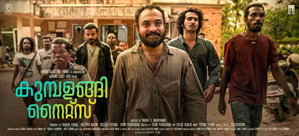 A group of men walk confidently through a rustic courtyard in a scene from the Malayalam film 'Kumbalangi Nights'. The central figure, with a beard and striped shirt, leads the group, surrounded by characters with diverse appearances, reflecting camaraderie and unity. The film's title is prominently displayed in Malayalam script, with production credits below.